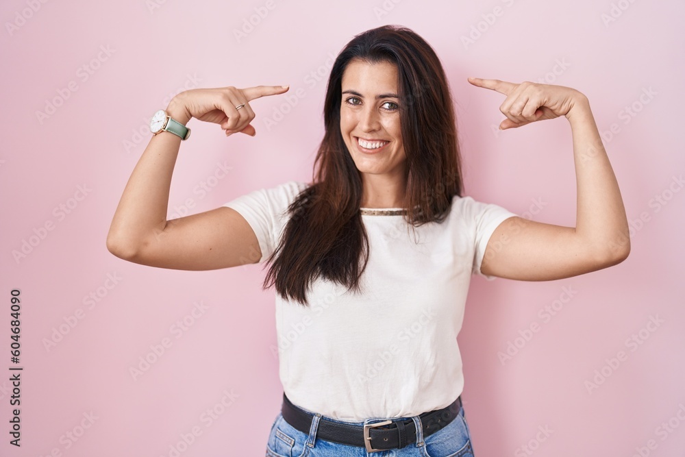 Young brunette woman standing over pink background smiling pointing to head with both hands finger, great idea or thought, good memory Young brunette woman standing over pink background smiling pointing to head with both hands finger, great idea or thought, good memory