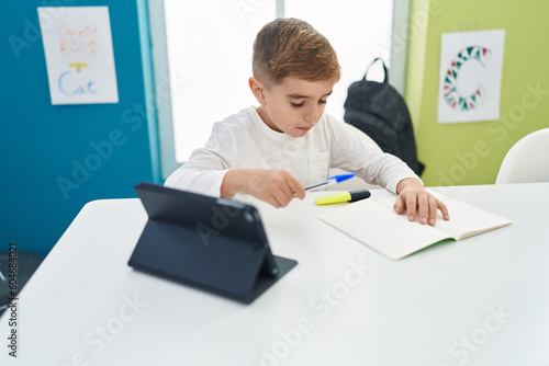 Adorable hispanic boy student using touchpad writing notes at classroom