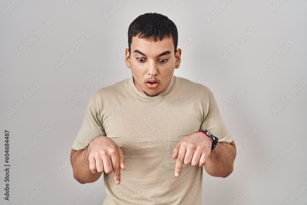 Young arab man wearing casual t shirt pointing down with fingers showing advertisement, surprised face and open mouth Young arab man wearing casual t shirt pointing down with fingers showing advertisement, surprised face and open mouth