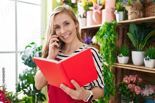Young blonde woman florist talking on smartphone reading book at flower shop
