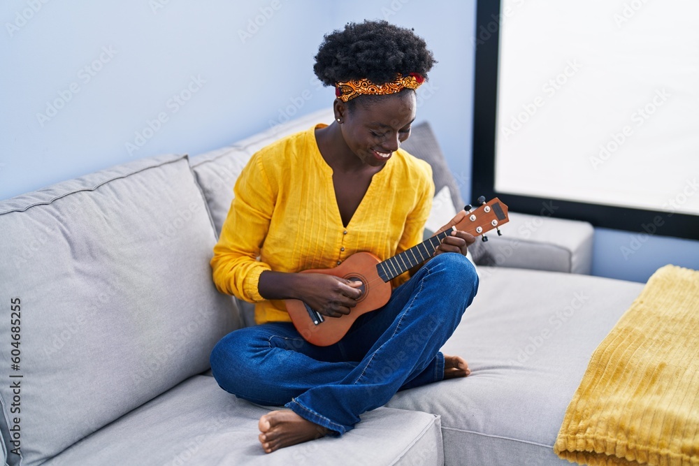 Young african american woman playing ukelele sitting on sofa at home