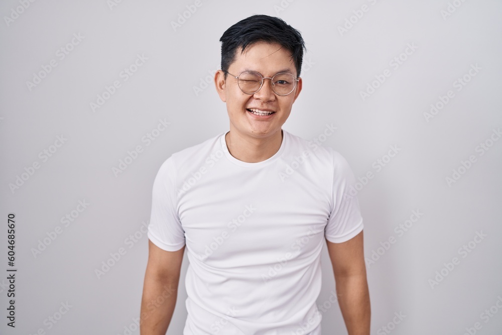 Young asian man standing over white background winking looking at the camera with sexy expression, cheerful and happy face. Young asian man standing over white background winking looking at the camera with sexy expression, cheerful and happy face.
