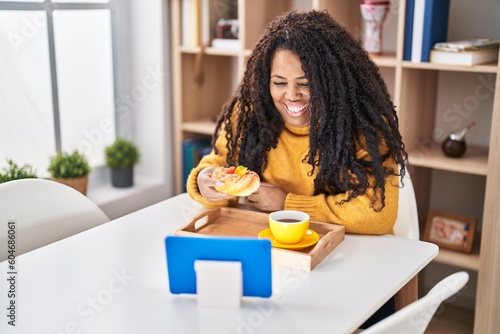 African american woman having breakfast watching video on touchpad at home
