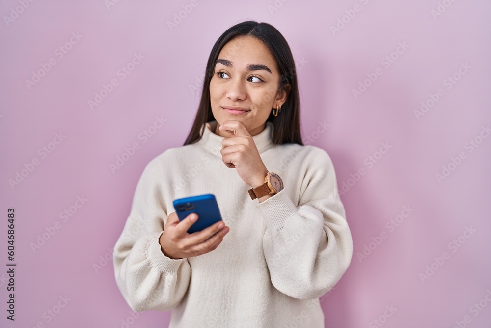 Young south asian woman using smartphone serious face thinking about question with hand on chin, thoughtful about confusing idea - obrazy, fototapety, plakaty 