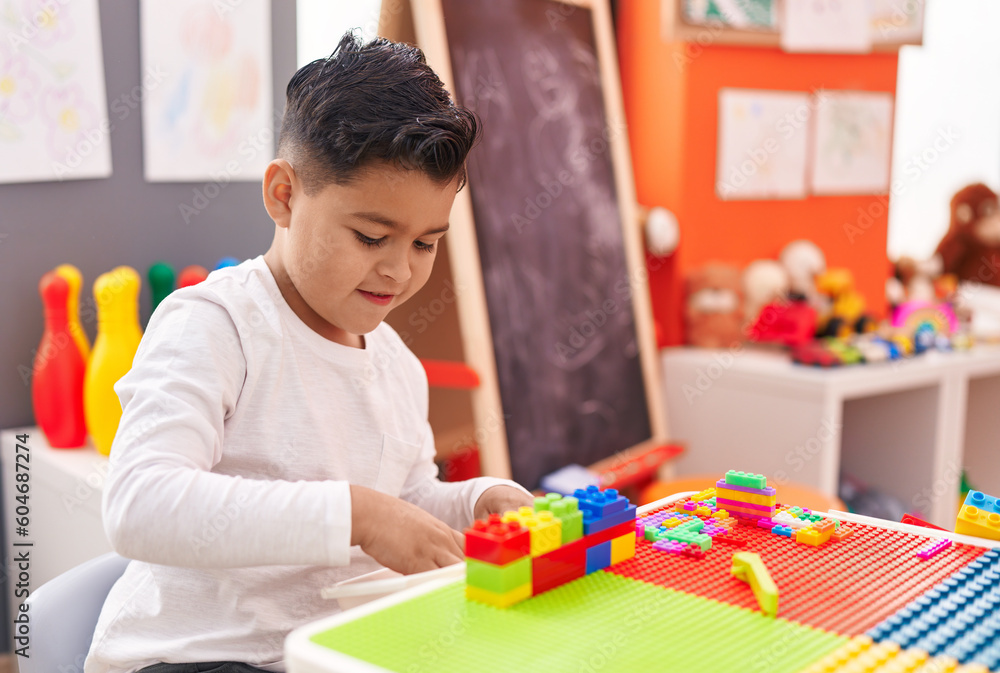 Adorable hispanic boy playing with construction blocks sitting on table at kindergarten Adorable hispanic boy playing with construction blocks sitting on table at kindergarten