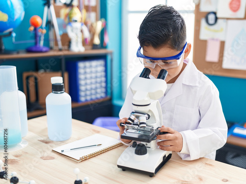 Adorable hispanic boy student using microscope at laboratory classroom