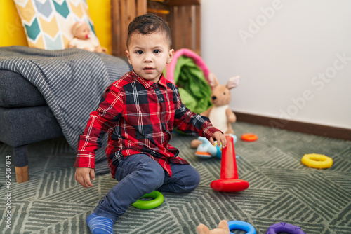Adorable hispanic boy playing with hoops game sitting on floor at home