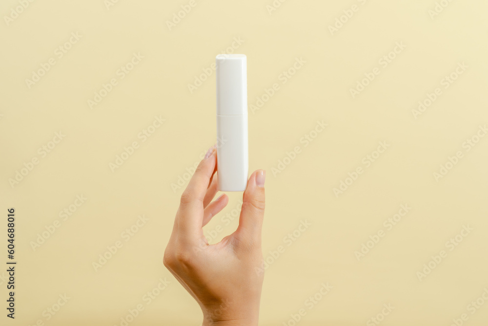 Womans hand holds a white tube (cream battle) for cosmetic products isolated on light background Womans hand holds a white tube (cream battle) for cosmetic products isolated on light background