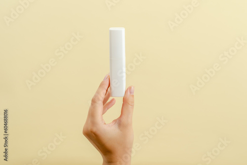 Womans hand holds a white tube (cream battle) for cosmetic products isolated on light background