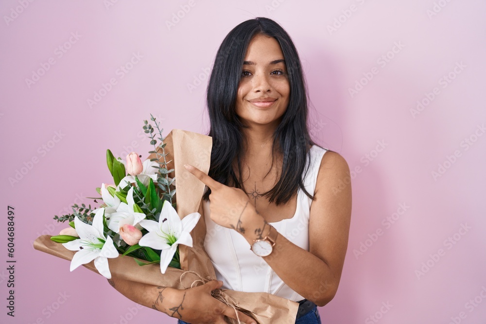 Brunette woman holding bouquet of white flowers pointing with hand finger to the side showing advertisement, serious and calm face Brunette woman holding bouquet of white flowers pointing with hand finger to the side showing advertisement, serious and calm face