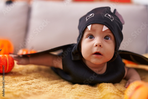 Adorable caucasian baby wearing bat costume lying on sofa at home