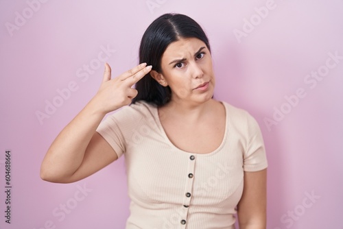 Young hispanic woman standing over pink background shooting and killing oneself pointing hand and fingers to head like gun  suicide gesture.