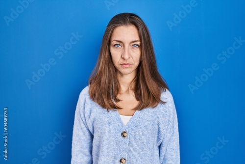 Young woman standing over blue background relaxed with serious expression on face. simple and natural looking at the camera.