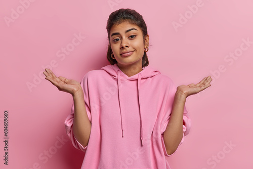 Photo Clueless indecisive Indian woman spreads palm shrugs shoulders looks clueless at