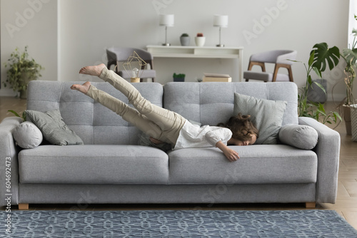 Obraz na plátně Adorable little girl enjoy carefree pastime at modern home, jump on cozy couch in living room, entertain on comfortable furniture, looks happy take pleasure on weekend