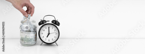 Womans hand put dollar bancnote into a glass jar with alarm clock photo