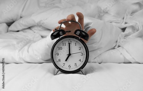 Woman's hand turning off black alarm clock on bed