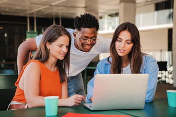 Group of multiracial happy teenage students using laptop, working on university assignment homework project in college library. Meeting of diverse young people looking information on computer. High