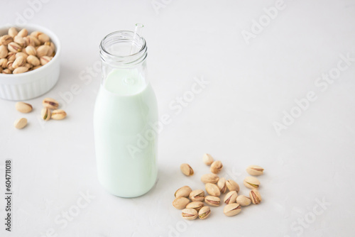 Pistachio milk in a bottle on a gray table next to pistachios. Vegetable milk. Nut milk for vegans