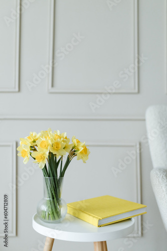 Bouquet of bright yellow daffodils on white wooden table together with yellow book with copy space