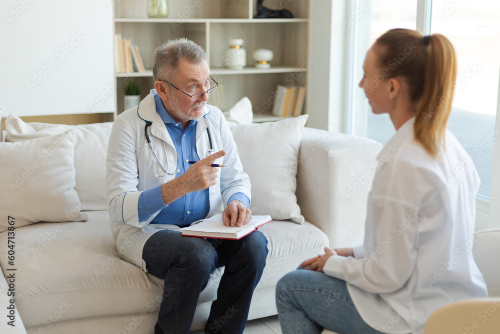 Senior man doctor examining yound woman in doctor office or at home. Girl patient and doctor have consultation in hospital room. Medicine healthcare medical checkup. Visit to doctor Senior man doctor examining yound woman in doctor office or at home. Girl patient and doctor have consultation in hospital room. Medicine healthcare medical checkup. Visit to doctor
