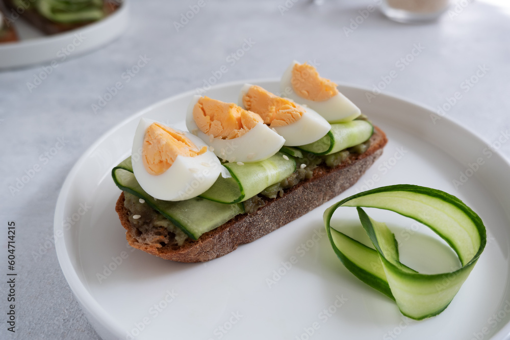 Toast with avocado, cucumber and egg on rye bread in a white plate on a light background. Healthy breakfast