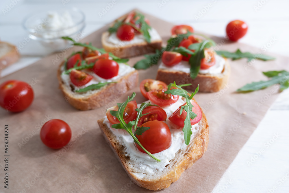 Cherry tomato toast with cream cheese and arugula on wheat bread on craft paper on a light background. Healthy breakfast, Proper nutrition. Cherry tomato toast with cream cheese and arugula on wheat bread on craft paper on a light background. Healthy breakfast, Proper nutrition.