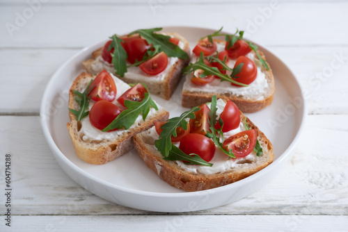 Cherry tomato toast with cream cheese and arugula on wheat bread in a white plate on a light background. Healthy breakfast, Proper nutrition.