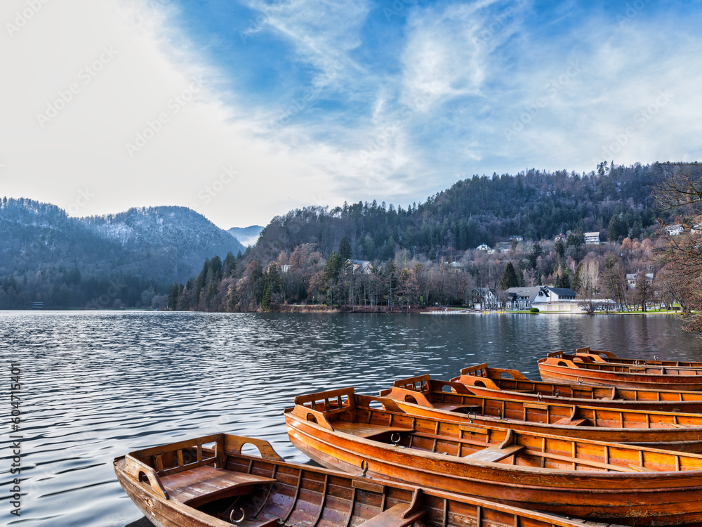 Wooden boats in Lake Bled and lakeside village during winter afternoon, Slovenia