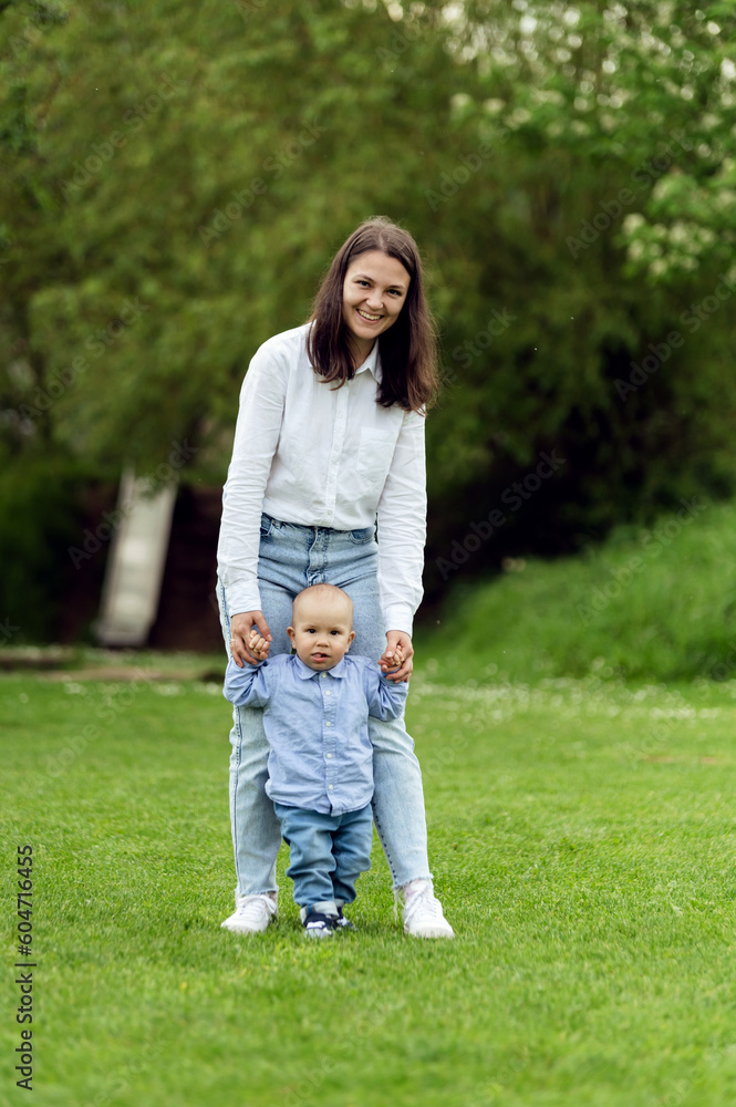 cute baby tries to take the first steps with the help of mom. the child holds his mother's hands and walks along the green lawn. cute baby tries to take the first steps with the help of mom. the child holds his mother's hands and walks along the green lawn.