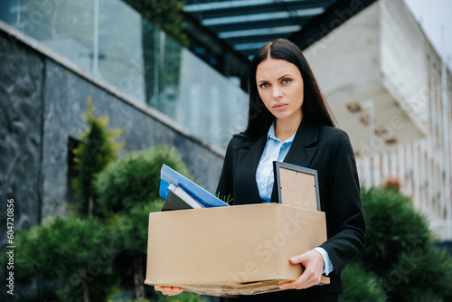 An unemployed woman carrying a box, depicting the loss of work and joblessness. Workless and Alone Woman Outside with Box of Belongings photo