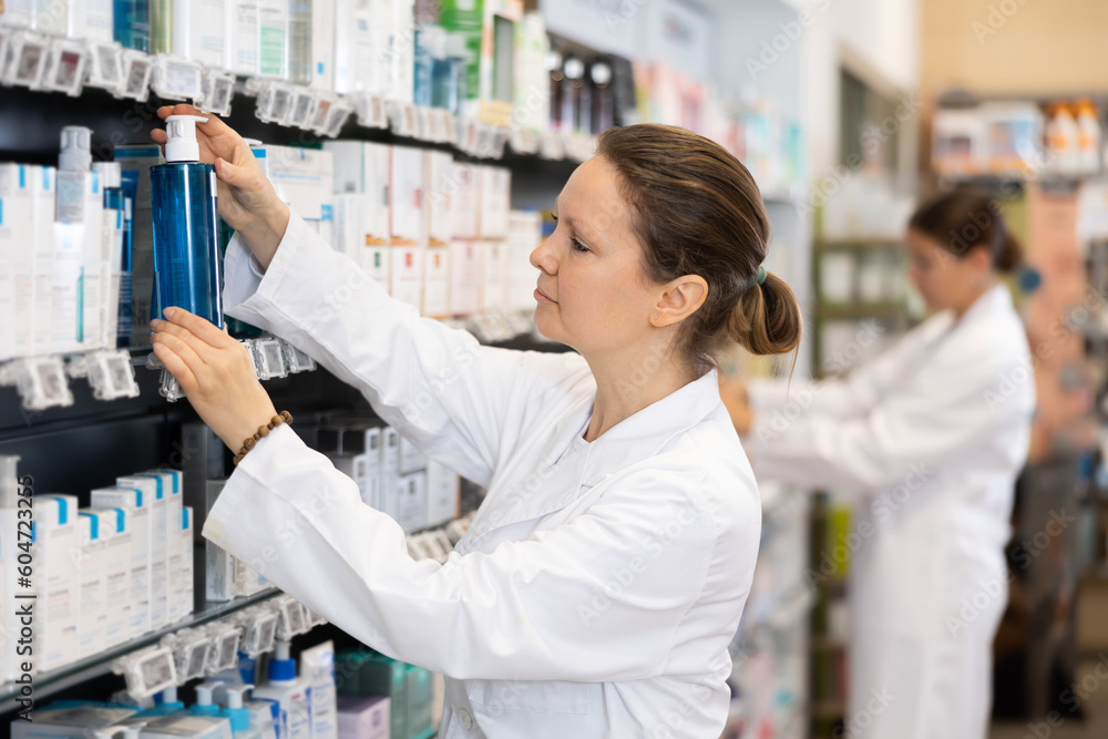 Adult woman pharmacist distributes assortment of goods on counter in pharmacy