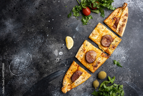 Sucuklu Pide Turkish Sausage pizza, on black dark stone table background, top view flat lay, with copy space for text