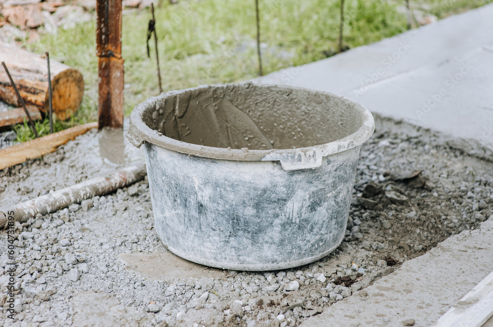 A bowl, a bucket, a concrete mixer in concrete, cement stands on stones at a construction site. Close-up photography.
