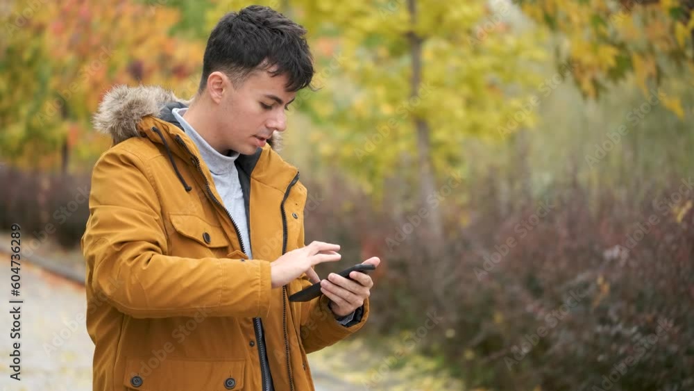 Smiling young man using a smart phone in a windy autumn day in the street. Smiling young man using a smart phone in a windy autumn day in the street.