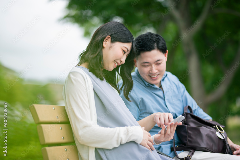 公園でスマートフォンを見る若い夫婦 公園でスマートフォンを見る若い夫婦
