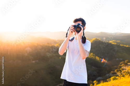 Photographer standing on top of a mountain taking pictures or filming the landscape of mountains with sunset.