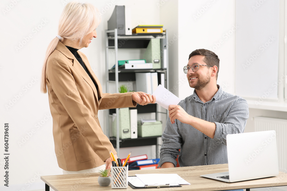 Boss giving paper card to employee in office