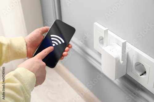 Woman with smartphone connecting to internet via wireless repeater indoors, closeup. Wi-Fi symbol on device screen photo