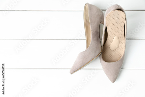 Orthopedic insoles in high heel shoes on white wooden floor, top view. Space for text