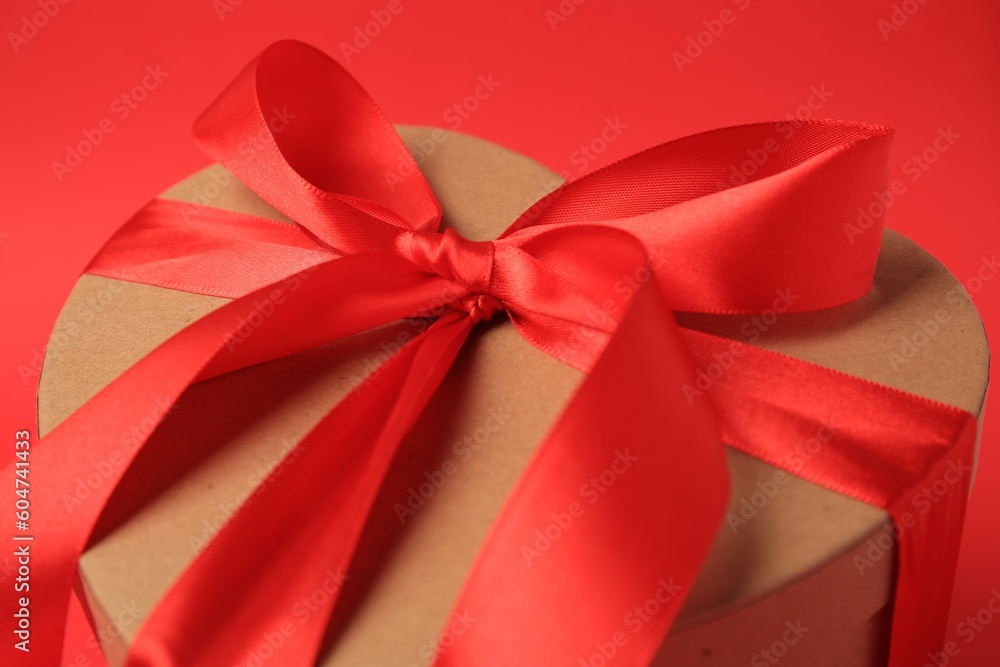 Beautiful heart shaped gift box with bow on red background, closeup Beautiful heart shaped gift box with bow on red background, closeup