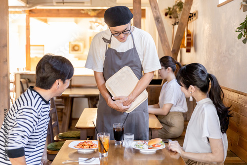 カフェ・飲食店で食べ物を運ぶお辞儀するホールスタッフ・店員と客 