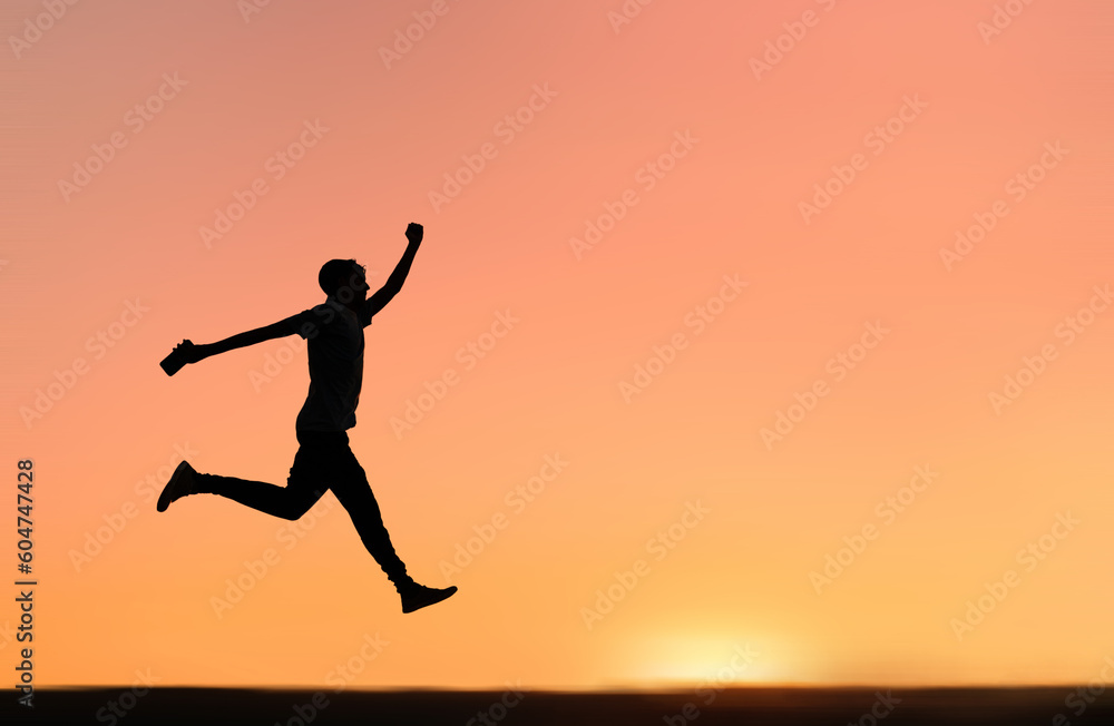 Silhouette of a happy man jumping  with the orange sunset sky in the background.  Concept of achieving success and life goals.