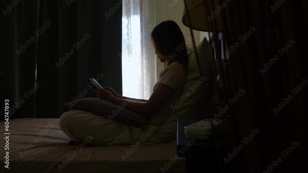 Depressed young Asian woman sitting on the bed and using mobile phone reading online message. Loneliness sad girl living alone with negative emotion and grief. Mental health and life problem concept. Depressed young Asian woman sitting on the bed and using mobile phone reading online message. Loneliness sad girl living alone with negative emotion and grief. Mental health and life problem concept.