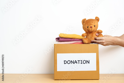 Kid Donation, Charity, Volunteer, Giving and Delivery Concept. Hand holding Bear doll and Clothes into Donation box at home for support and help poor, refugee and homeless people. Copy space for text © Jo Panuwat D