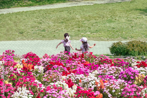 満開の花壇のそばを楽しげに走り回る二人の少女