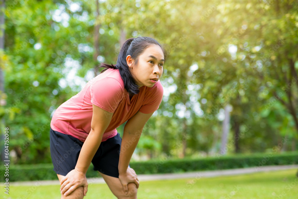 Young Asian woman standing bent over and breathing after running in the park. Young healthy woman taking a break after running. Healthy lifestyle concept. Young Asian woman standing bent over and breathing after running in the park. Young healthy woman taking a break after running. Healthy lifestyle concept.