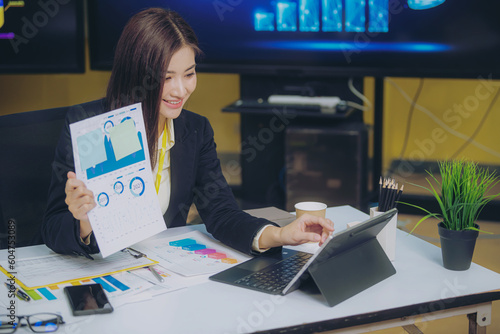 Businesswoman holding graph to analyze marketing plan turnover and profit Tax calculation with calculator and laptop on wooden table in office