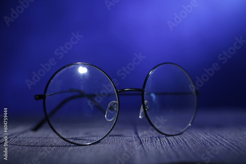 Spectacless or eyeglasses on wooden table under dark blue light