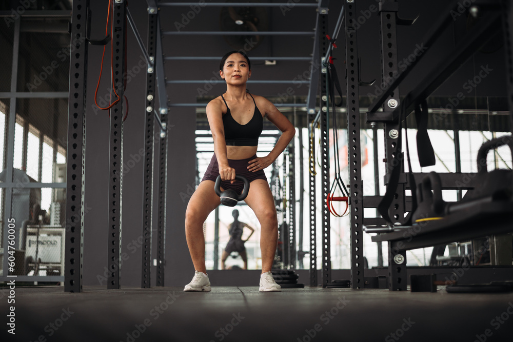 Strong Asian woman doing exercise with kettlebell at cross fit gym. Athlete female wearing sportswear workout on grey gym background with weight and dumbbell equipment. Healthy lifestyle. Strong Asian woman doing exercise with kettlebell at cross fit gym. Athlete female wearing sportswear workout on grey gym background with weight and dumbbell equipment. Healthy lifestyle.